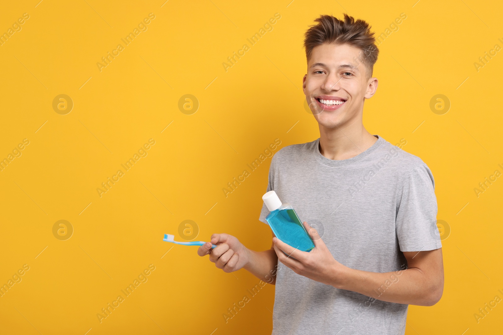 Photo of Young man with mouthwash and toothbrush on yellow background, space for text