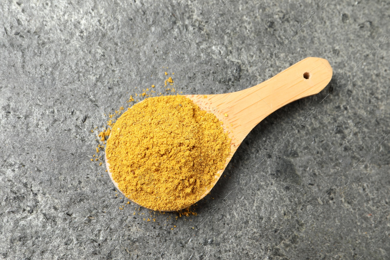 Photo of Spoon with dry curry powder on dark textured table, top view