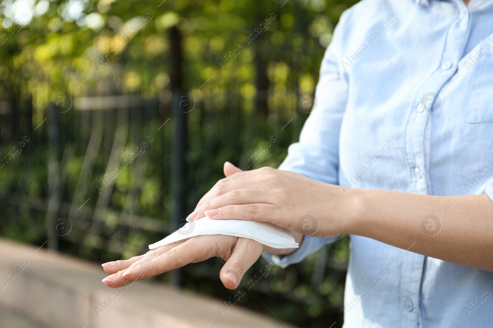 Photo of Woman cleaning hands with antiseptic wipe outdoors, closeup. Virus prevention