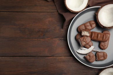 Photo of Delicious milk chocolate candy bars with coconut filling on wooden table, flat lay. Space for text