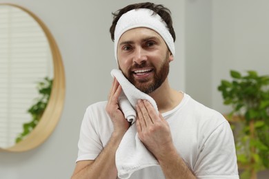 Photo of Washing face. Man with headband and towel in bathroom