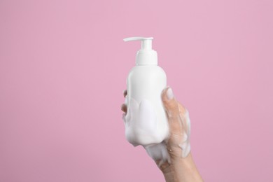 Photo of Woman with foam on hand holding bottle of skin cleanser against pink background, closeup. Cosmetic product