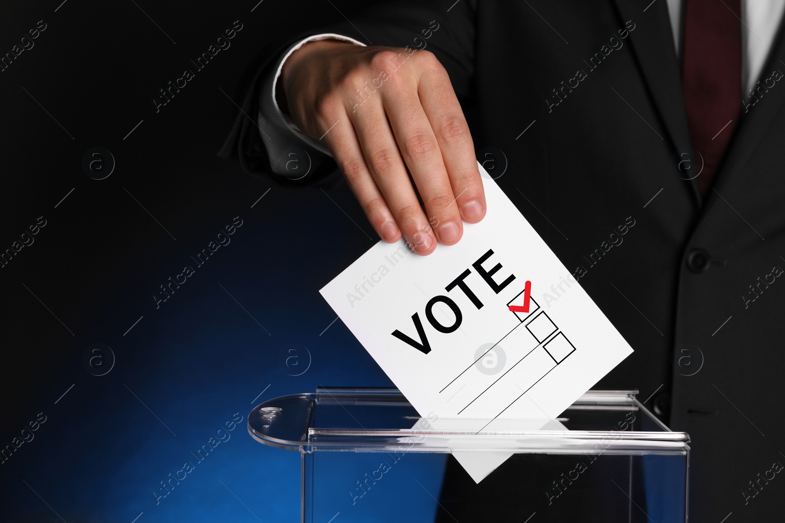 Image of Man putting paper with word Vote and tick into ballot box on dark blue background