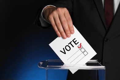 Image of Man putting paper with word Vote and tick into ballot box on dark blue background