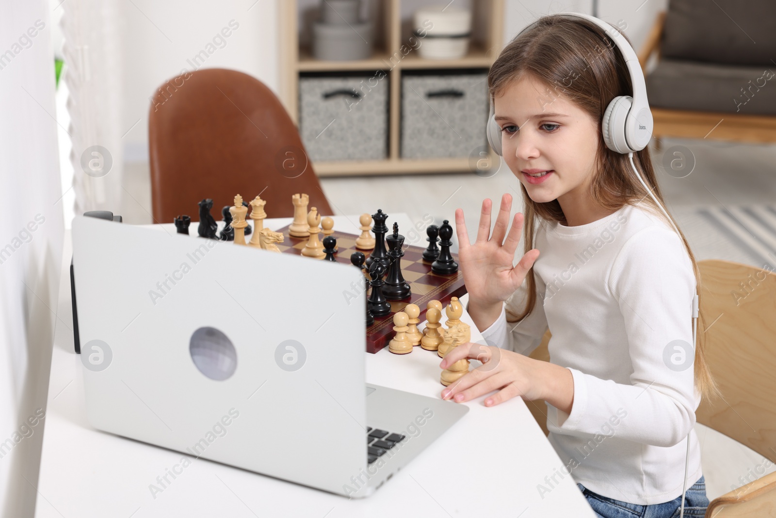 Photo of Cute girl learning to play chess with online tutor at home