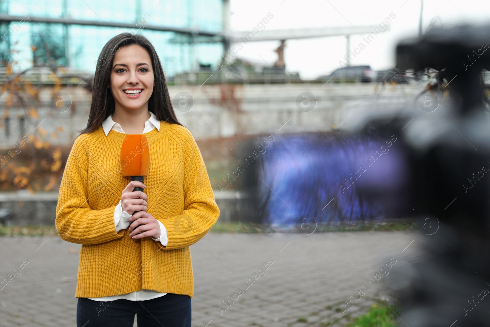 Photo of Young female journalist with microphone working on city street