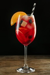 Photo of Glass of Red Sangria on wooden table against black background