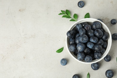 Photo of Bowl of tasty blueberries and leaves on light table, top view with space for text