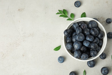 Bowl of tasty blueberries and leaves on light table, top view with space for text