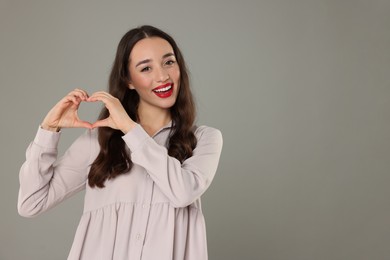 Photo of Beautiful young woman making heart with hands on grey background, space for text