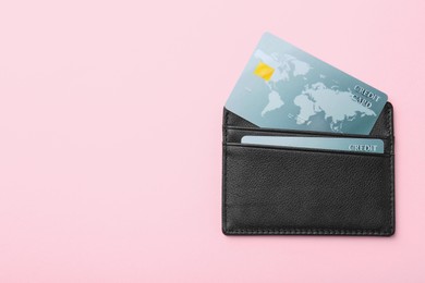 Leather card holder with credit cards on pink background, top view. Space for text