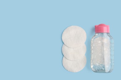 Photo of Bottle of makeup remover and cotton pads on light blue background, flat lay. Space for text