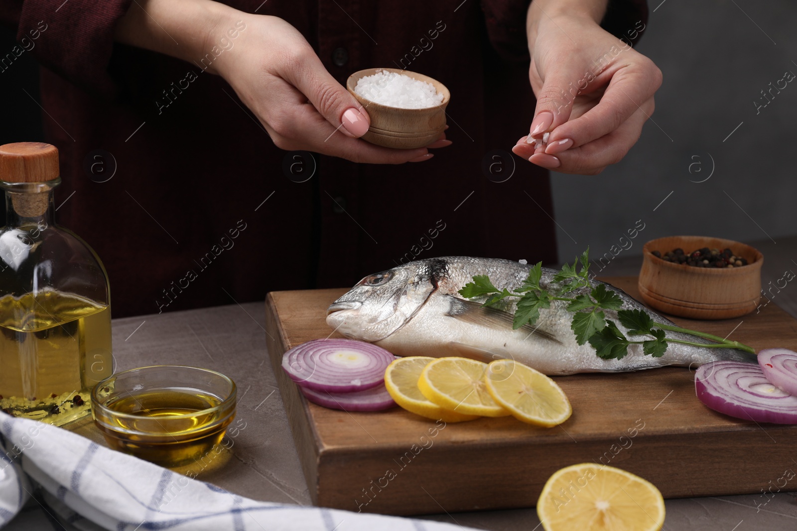 Photo of Woman salting raw dorado fish at grey table, closeup