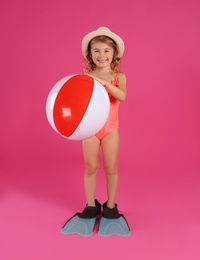 Cute little child in beachwear with bright inflatable ball on pink background