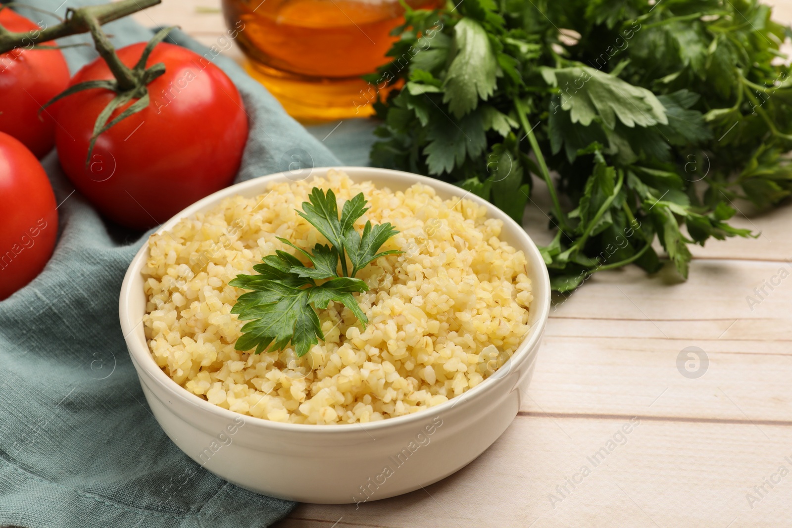 Photo of Delicious bulgur with parsley in bowl and tomatoes on wooden table, closeup