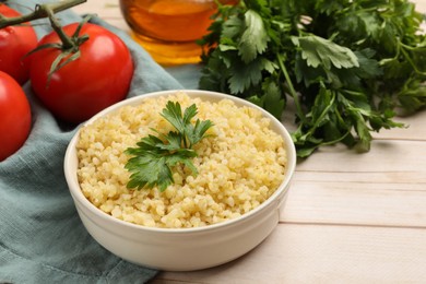 Delicious bulgur with parsley in bowl and tomatoes on wooden table, closeup