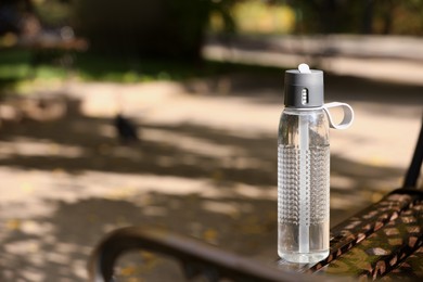 Sport bottle of water on wooden bench in park, space for text