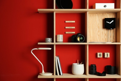 Stylish wooden shelves with photography equipment and decorative elements on red wall