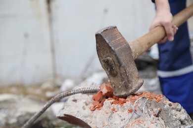 Man breaking brick with sledgehammer outdoors, selective focus. Space for text