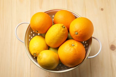 Photo of Colander with fresh citrus fruits on wooden table, top view