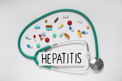 Word Hepatitis, stethoscope, and pills on white background, flat lay