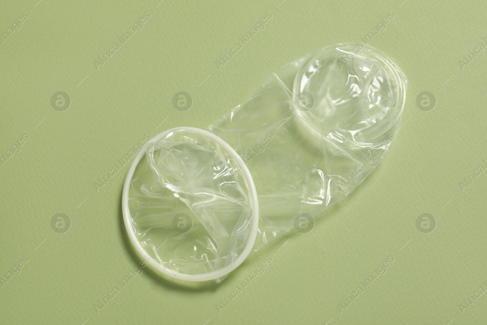 Photo of Unrolled female condom on light green background, top view. Safe sex