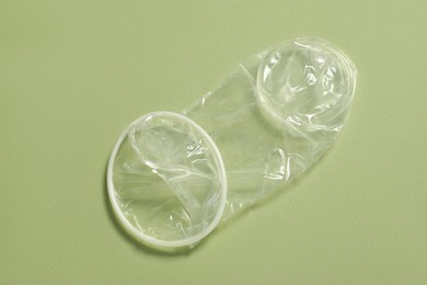 Unrolled female condom on light green background, top view. Safe sex