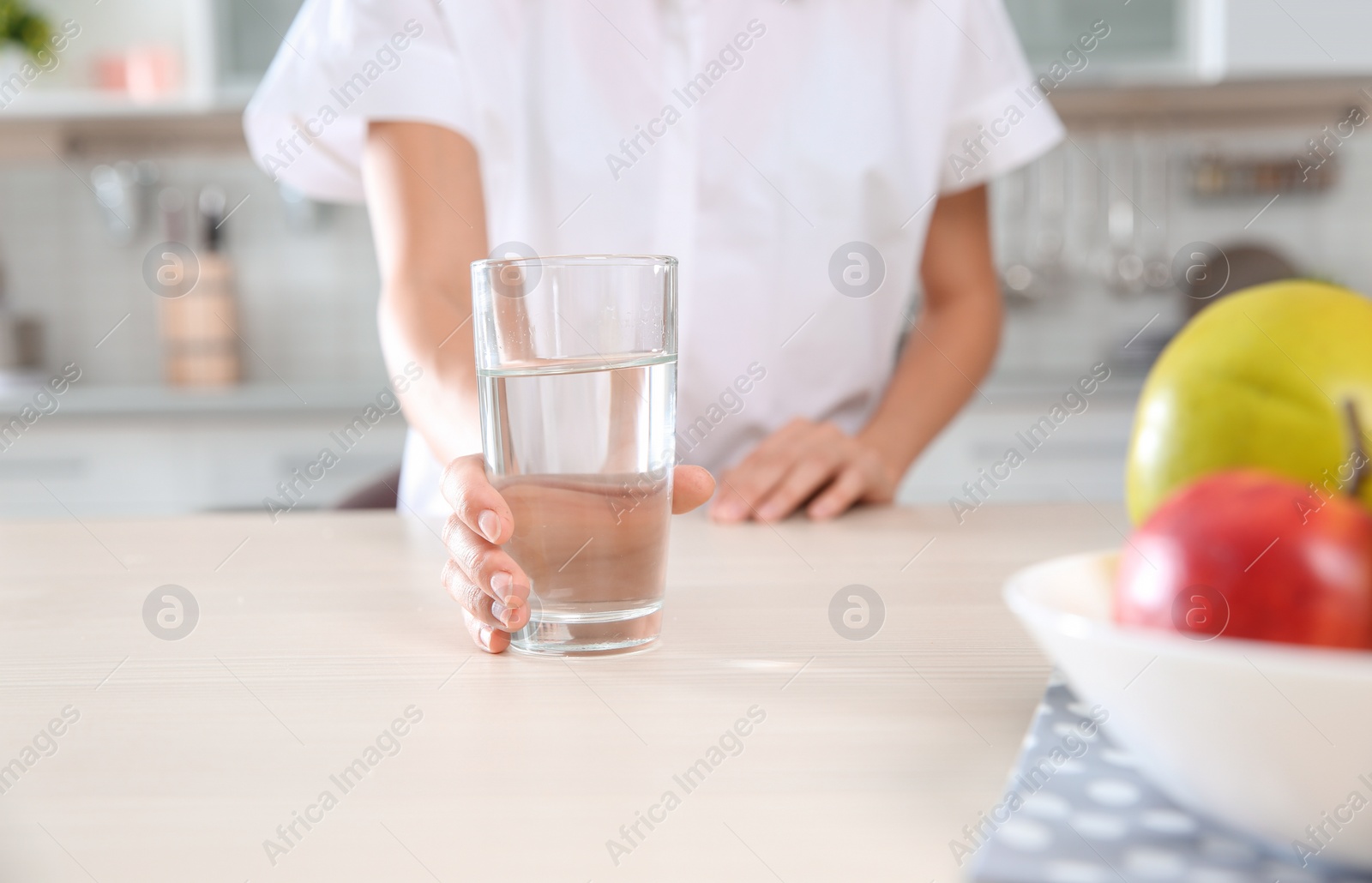 Photo of Woman holding glass with clean water on table in kitchen, closeup