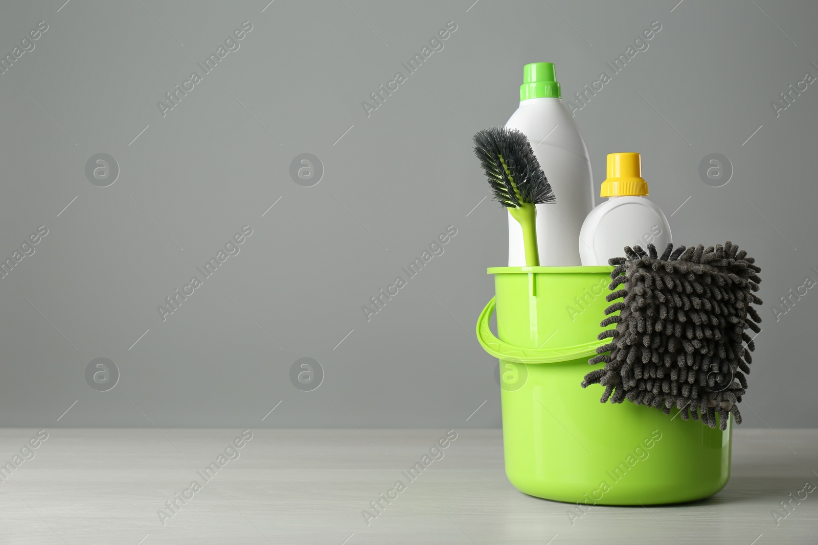 Photo of Bucket with cleaning products and tools on grey table. Space for text