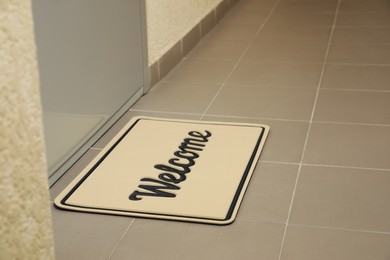 Photo of Beautiful beige doormat with word Welcome on floor near entrance