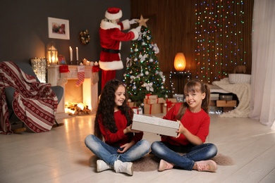 Photo of Little children with gift and Santa Claus decorating Christmas tree at home