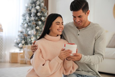 Couple holding gift box in room with Christmas tree