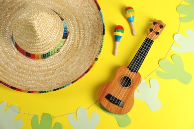 Mexican sombrero hat, maracas, ukulele and garland on yellow background, flat lay