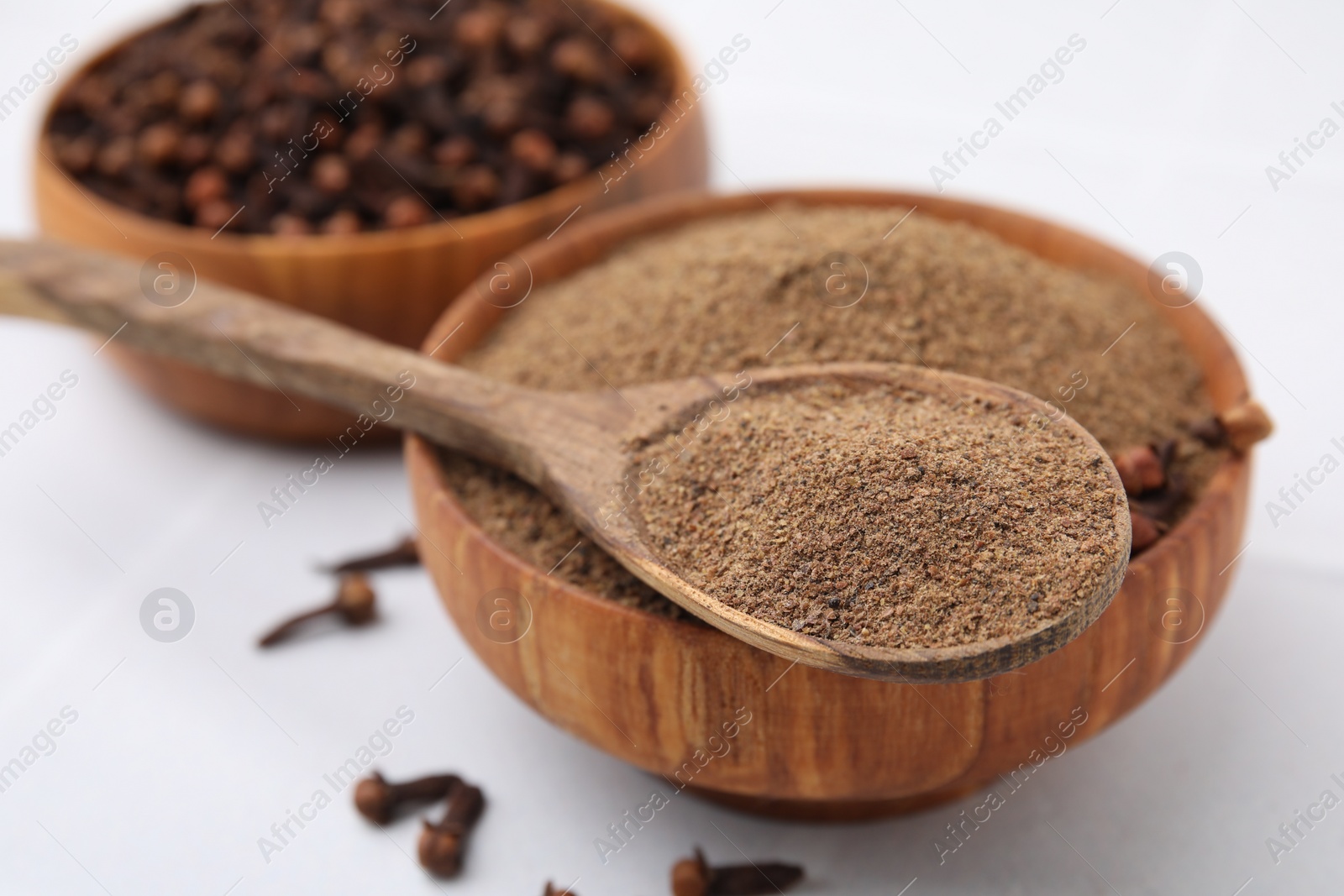 Photo of Aromatic clove powder in bowl, dried buds and spoon on white table, closeup