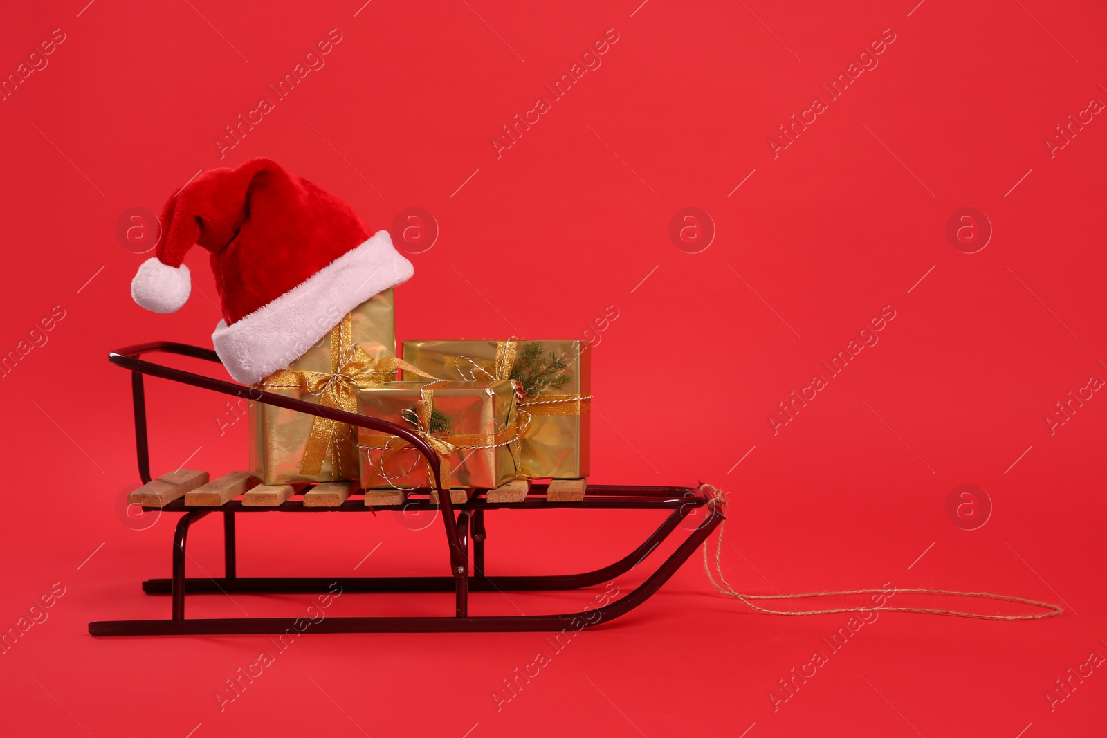 Photo of Sleigh with gift boxes and Santa hat on red background. Space for text