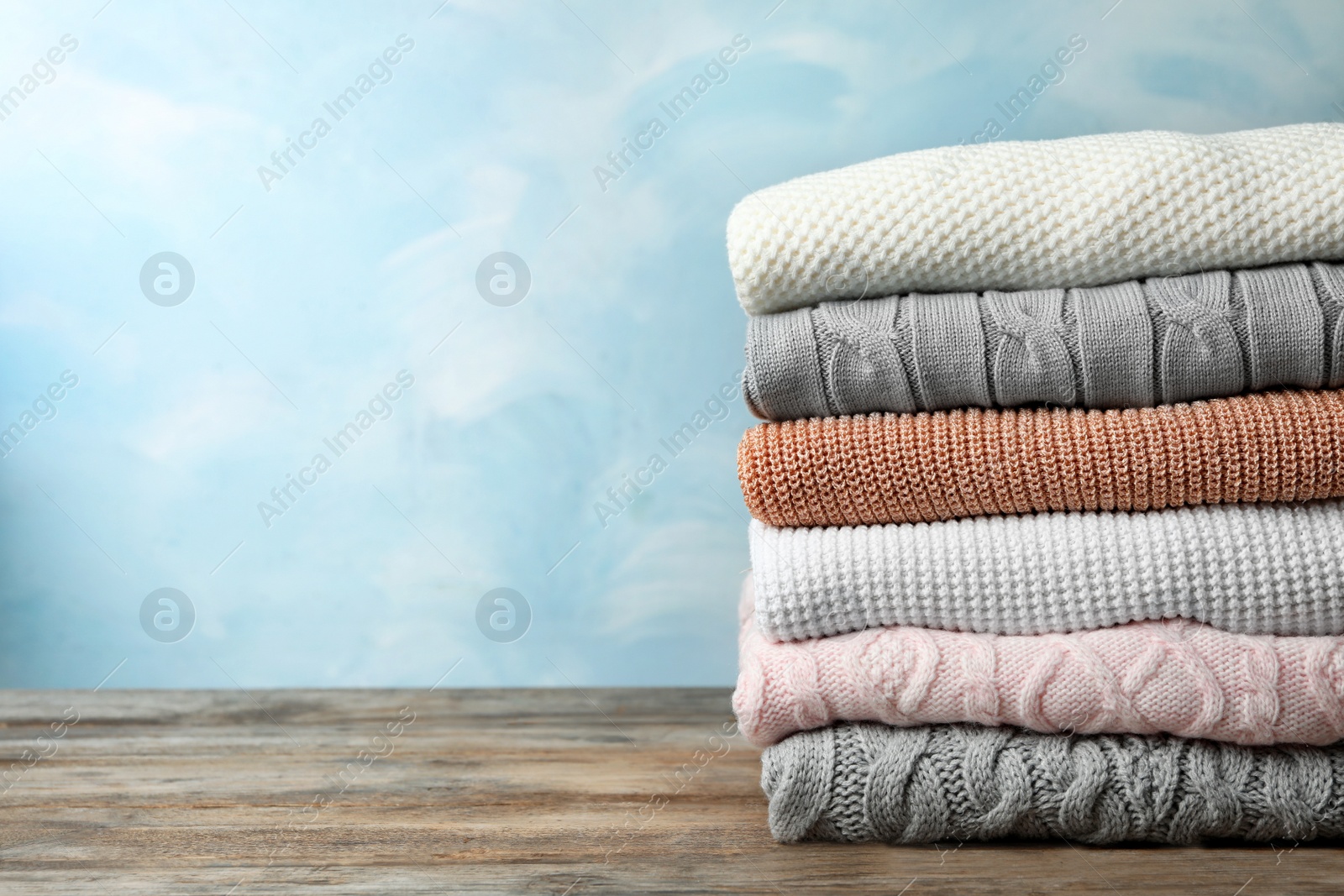 Photo of Stack of warm clothes on wooden table against light blue background, space for text. Autumn season