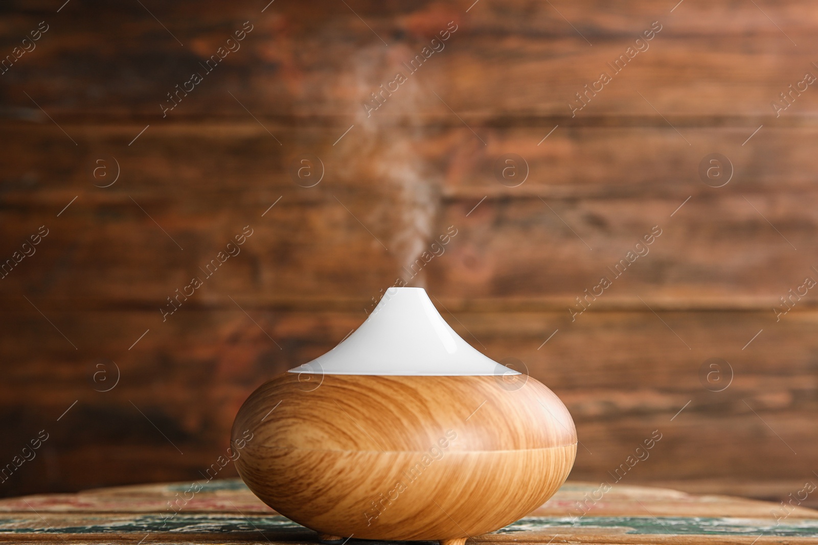 Photo of Modern essential oil diffuser on wooden table against brown background