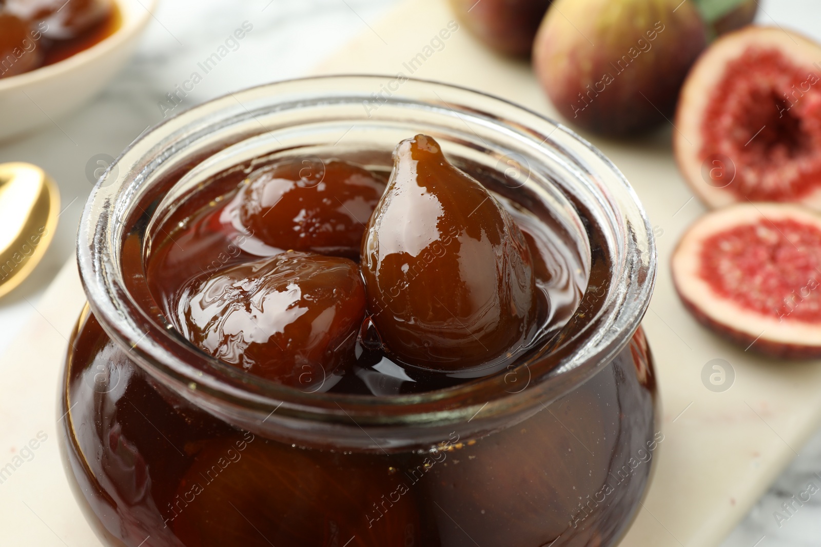 Photo of Jar of tasty sweet fig jam on white marble table, closeup
