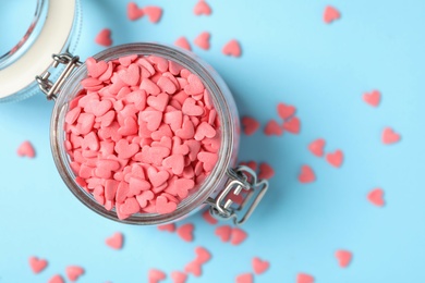 Photo of Bright heart shaped sprinkles and glass jar on light blue background, flat lay. Space for text