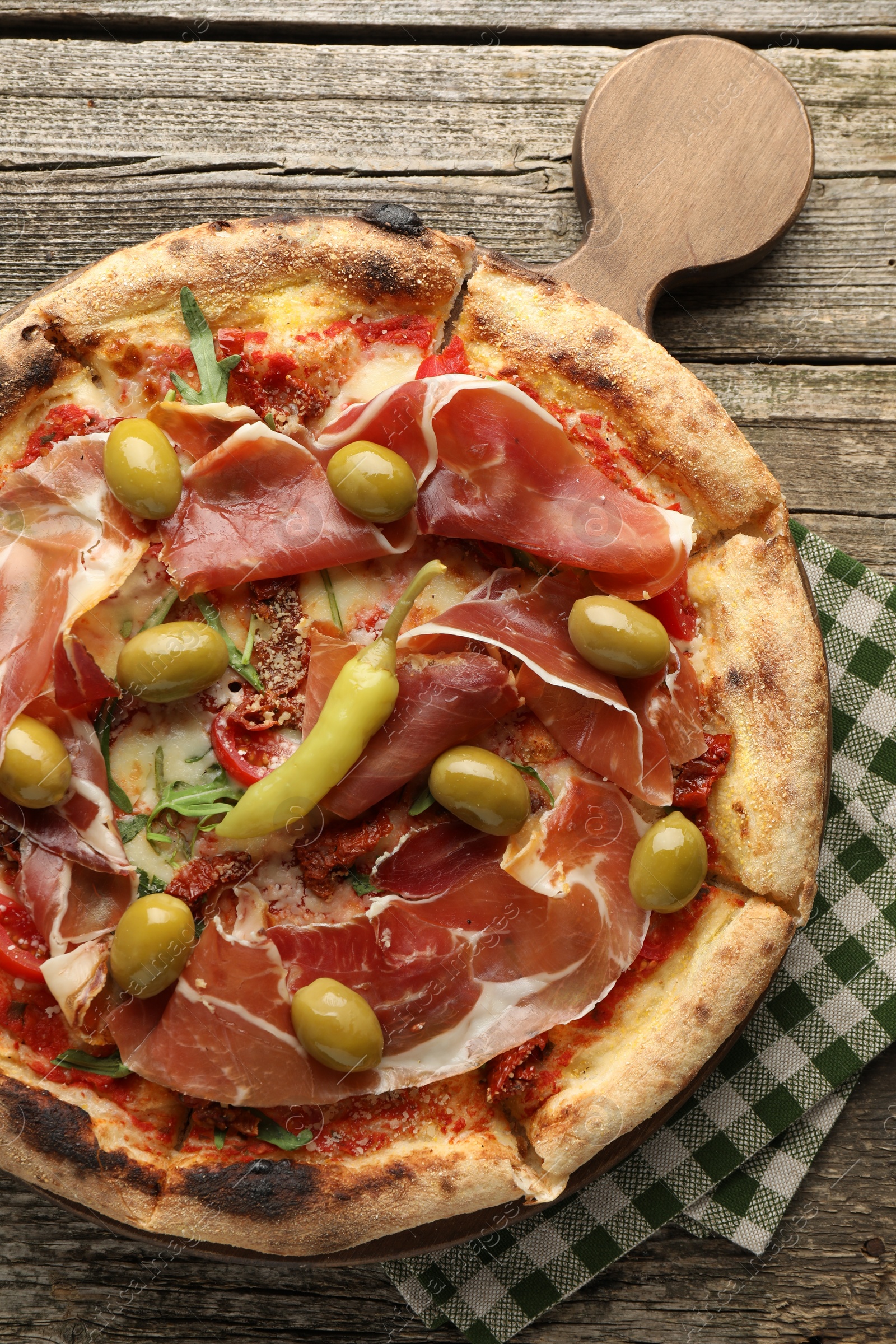 Photo of Tasty pizza with cured ham, olives, sun-dried tomato and pepper on wooden table, top view