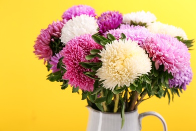 Photo of Beautiful asters in jug on yellow background, closeup. Autumn flowers