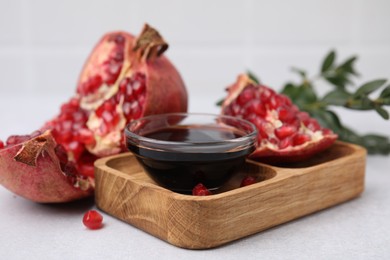 Photo of Tasty pomegranate sauce in bowl and fruits on light table, closeup