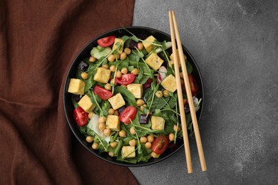 Photo of Bowl of tasty salad with tofu, chickpeas and vegetables on brown textured table, top view