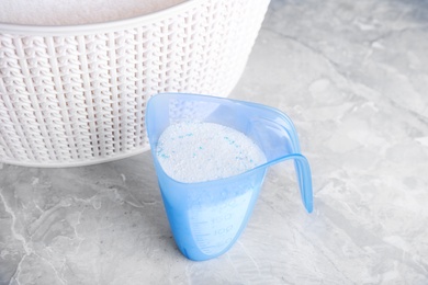 Photo of Measuring cup of washing powder and plastic laundry basket on marble table