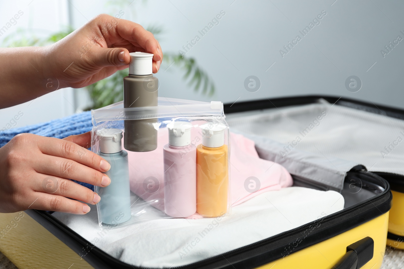 Photo of Woman with plastic bag of cosmetic travel kit packing suitcase, closeup