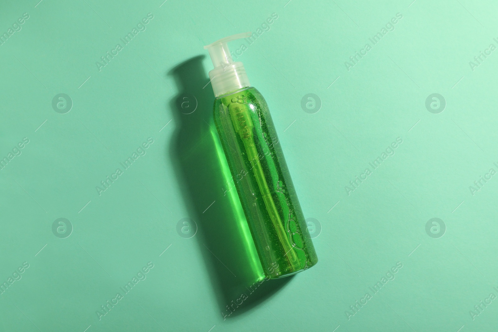 Photo of Bottle of green cosmetic gel on turquoise background, top view
