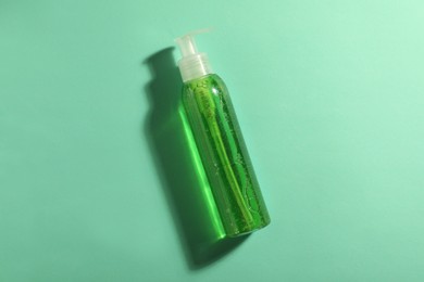 Bottle of green cosmetic gel on turquoise background, top view
