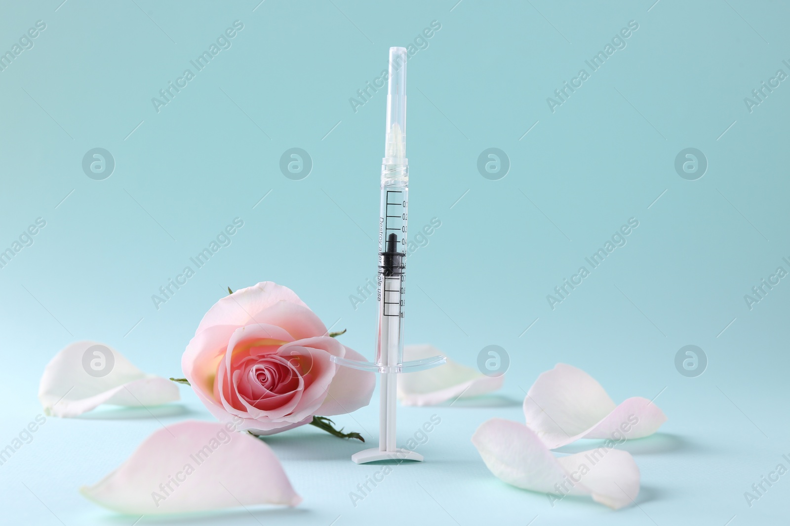 Photo of Cosmetology. Medical syringe, rose flower and petals on light blue background