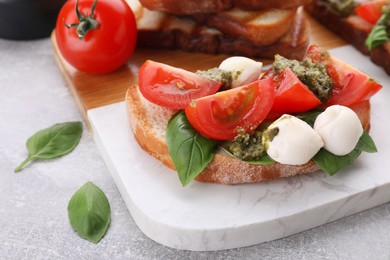 Photo of Delicious Caprese sandwich with mozzarella, tomatoes, basil and pesto sauce on light grey table, closeup