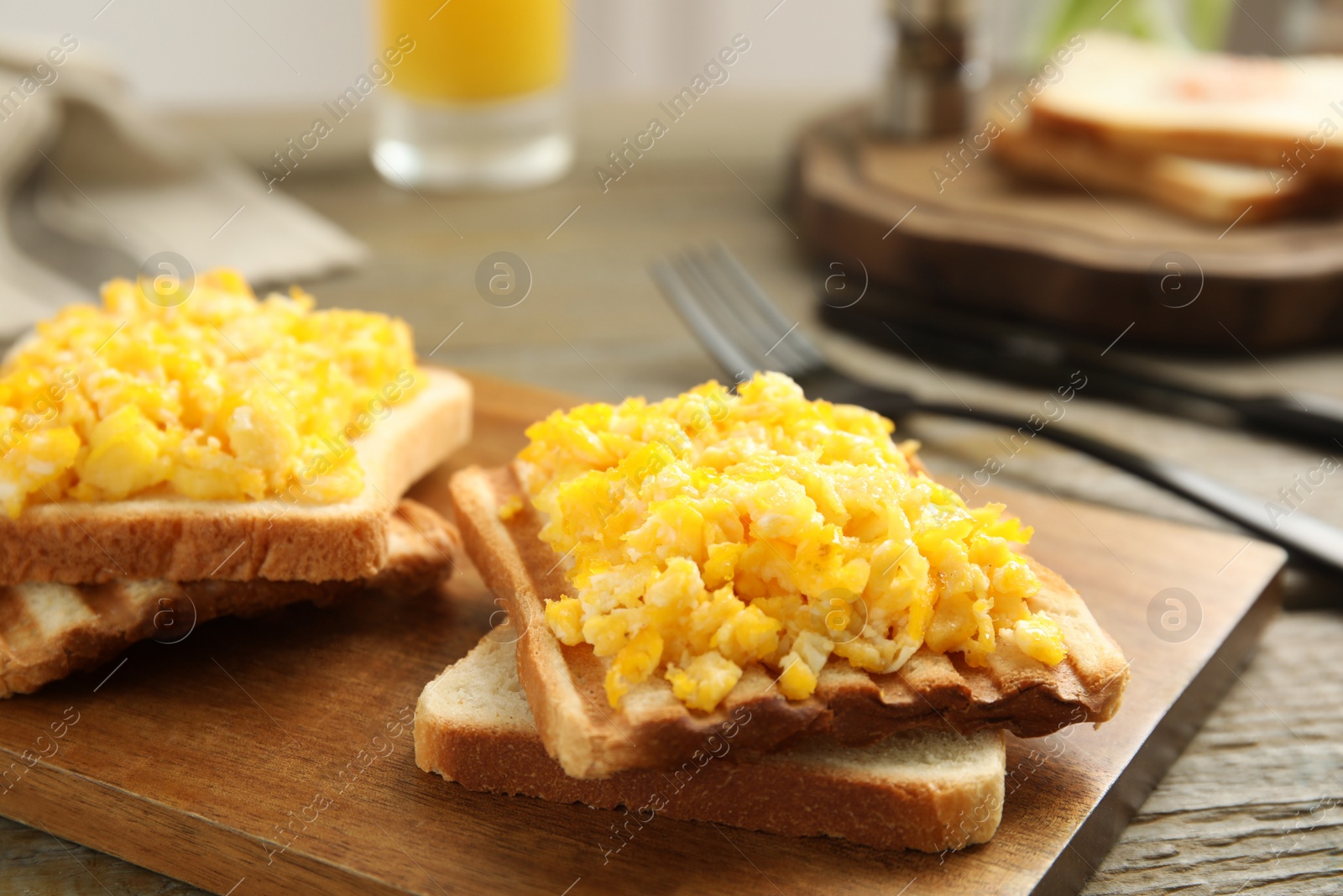 Photo of Delicious breakfast with scrambled eggs and toasted bread served on wooden board, closeup